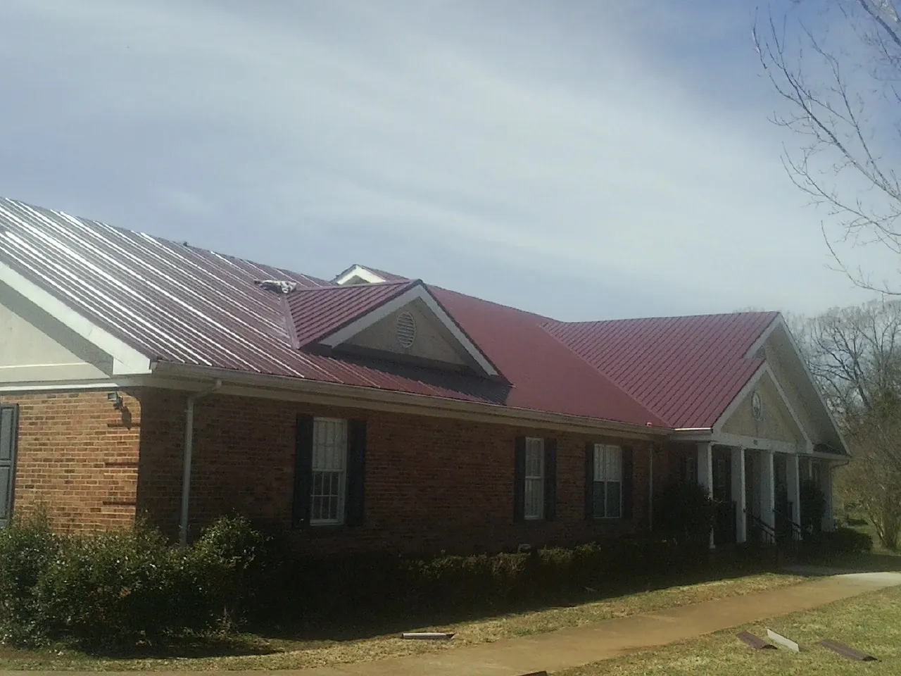 Red metal roof with gabled entries on a long brick building, from a Hail Damage Roof Repair job in Middle Haddam