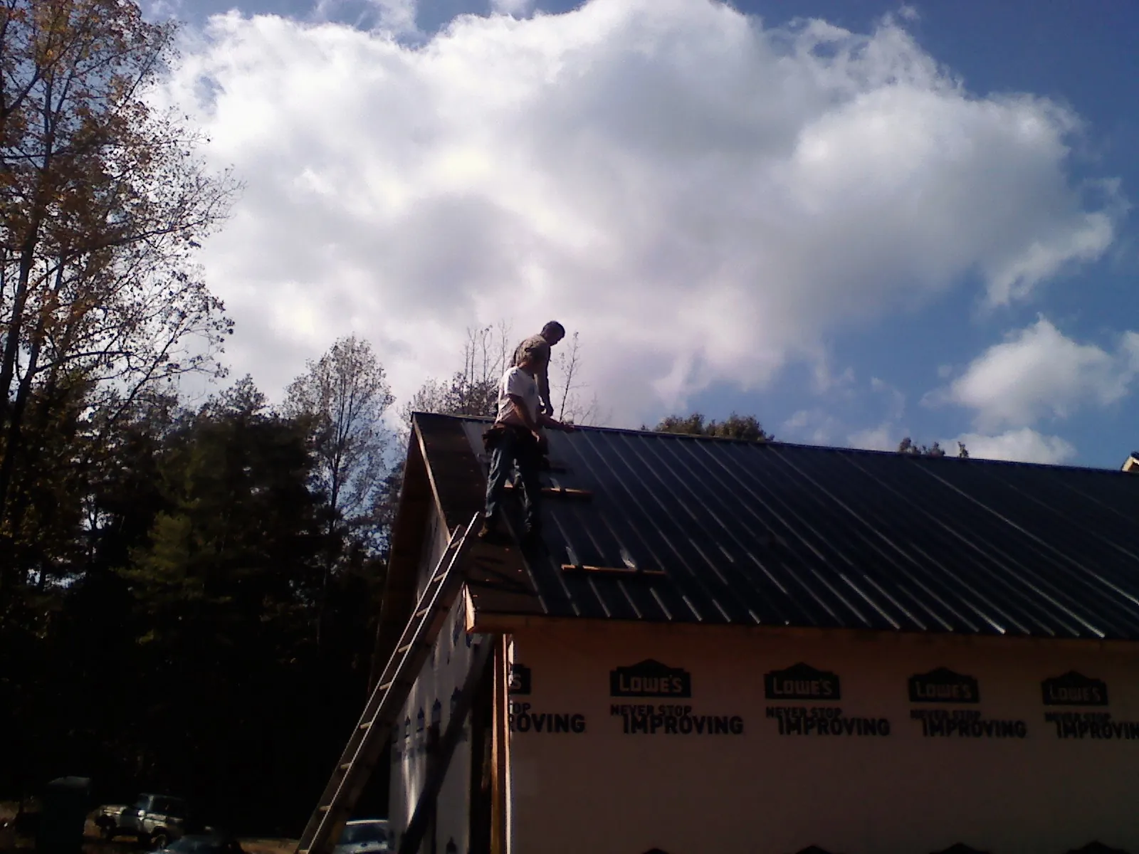 Roofer fastening dark metal panels high against a cloudy sky, from a Roof Inspection job in Middle Haddam