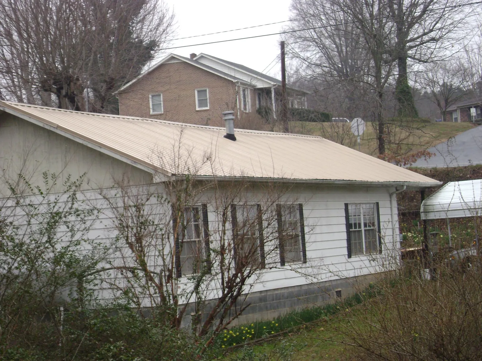Tan metal roof on a white sided house set into a hillside — Commercial Roofing by Roofing Brothers in Middle Haddam